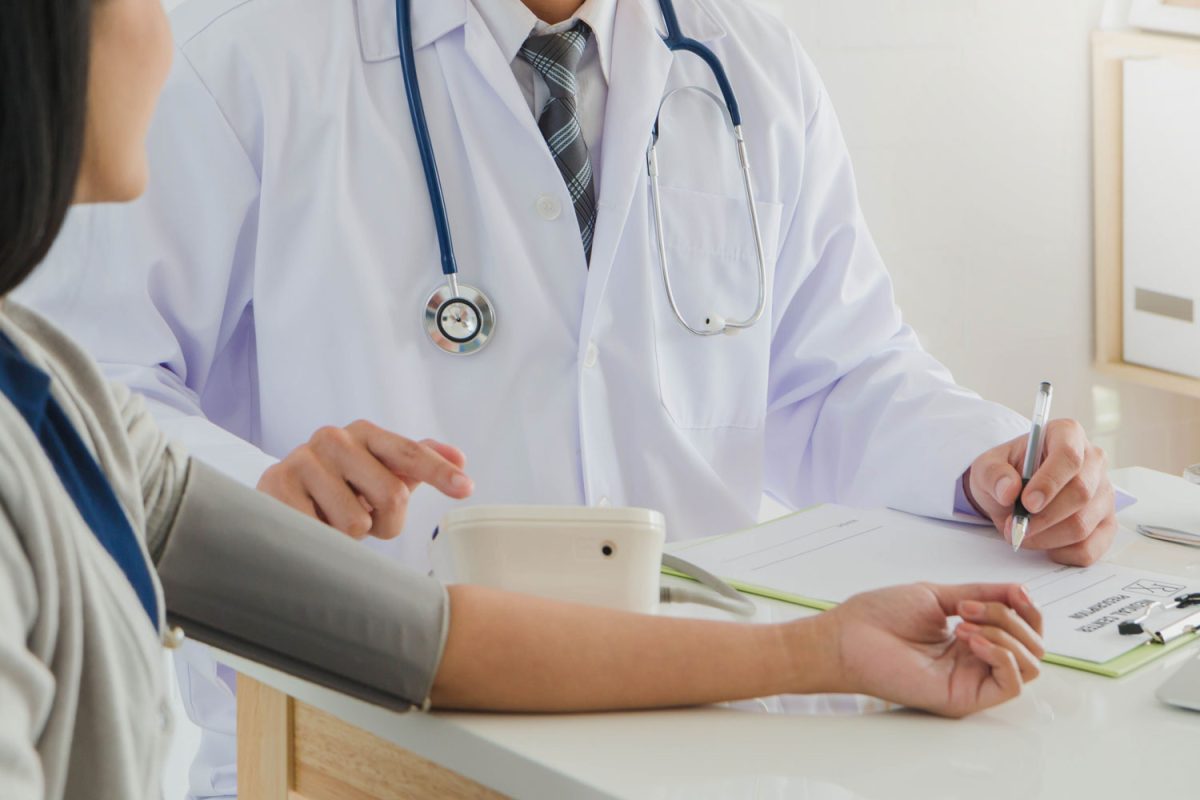 Professional doctor wearing white coat is checking woman patient with stethoscope and measure blood pressure in hospital background.Concept of