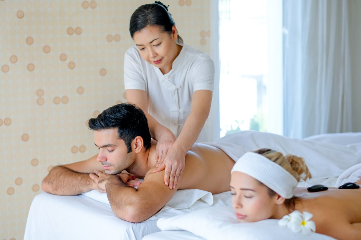 Handsome man enjoy with Thai masseuse massage to him and he lie on bed with his girlfriend in spa room with day light.