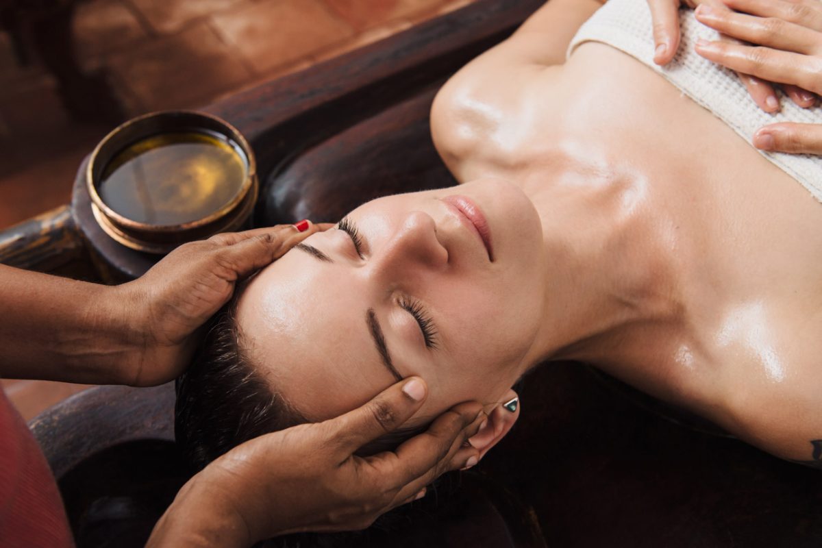 Ayurvedic face massage with oil on the wooden table in traditional style made by Asian women.