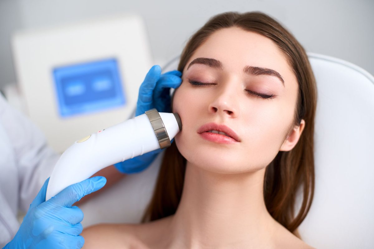 Beautician doctor doing rf-lifting procedure for flawless woman face laying in a beauty salon. Hardware cosmetology. Patient receiving electric facial massage. Skin rejuvenation and wrinkle smoothing.