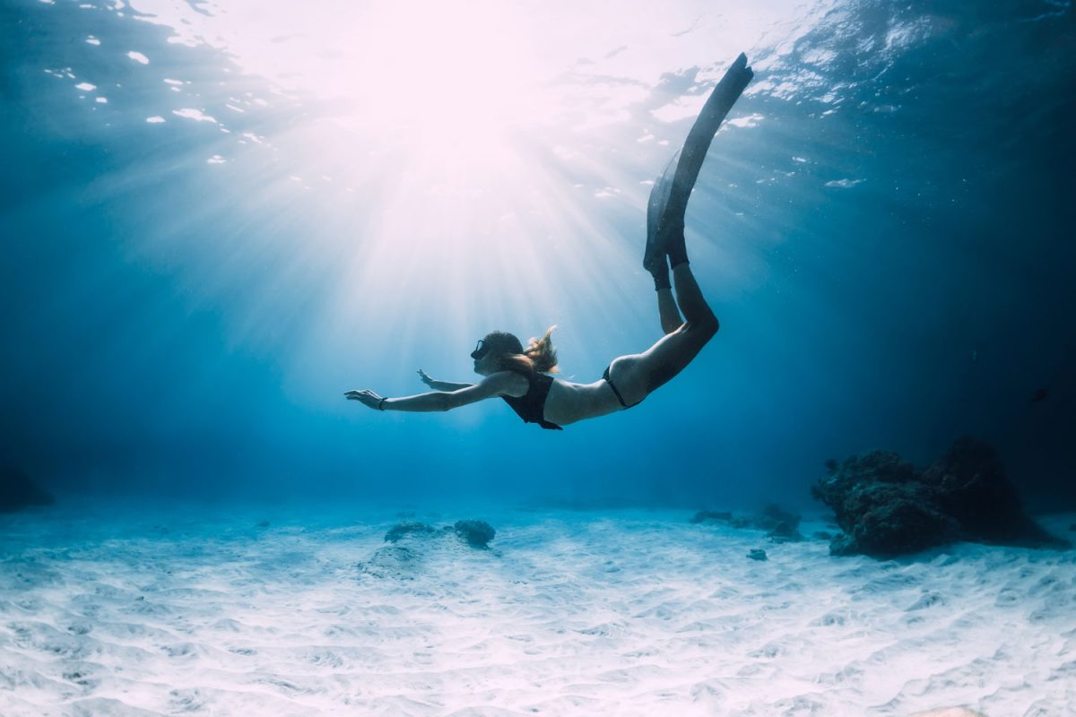 Woman freediver glides with fins. over sandy sea. Freediving and beautiful sunlight in blue ocean