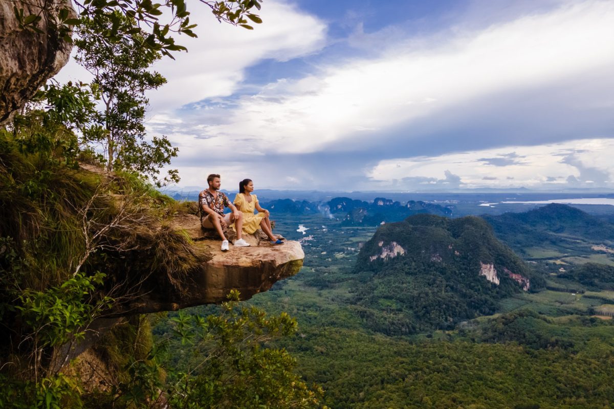 Couple at the edge of a mountain, Dragon Crest mountain Krabi Thailand, Young travelers sits on a rock that overhangs the abyss, with a beautiful landscape. Dragon Crest or Khuan Sai at Khao Ngon Nak